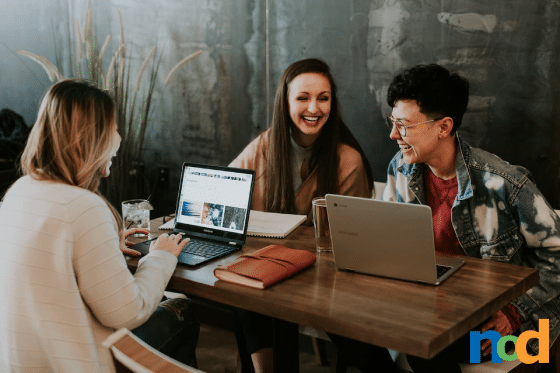 People sitting at a table on their laptops laughing together