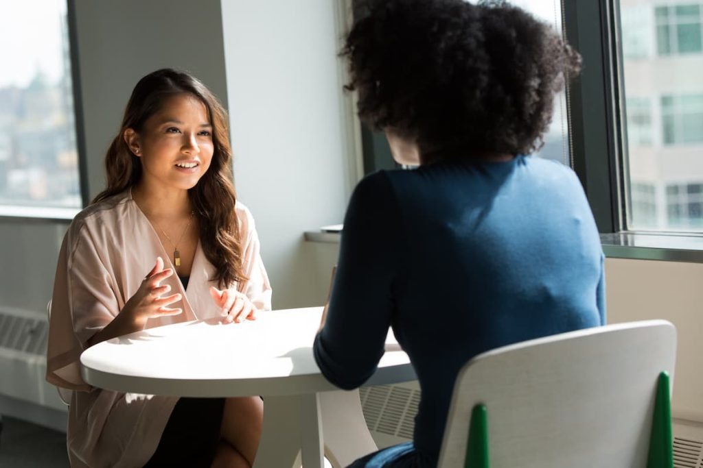 Two women sitting at a table in the sunlight chatting