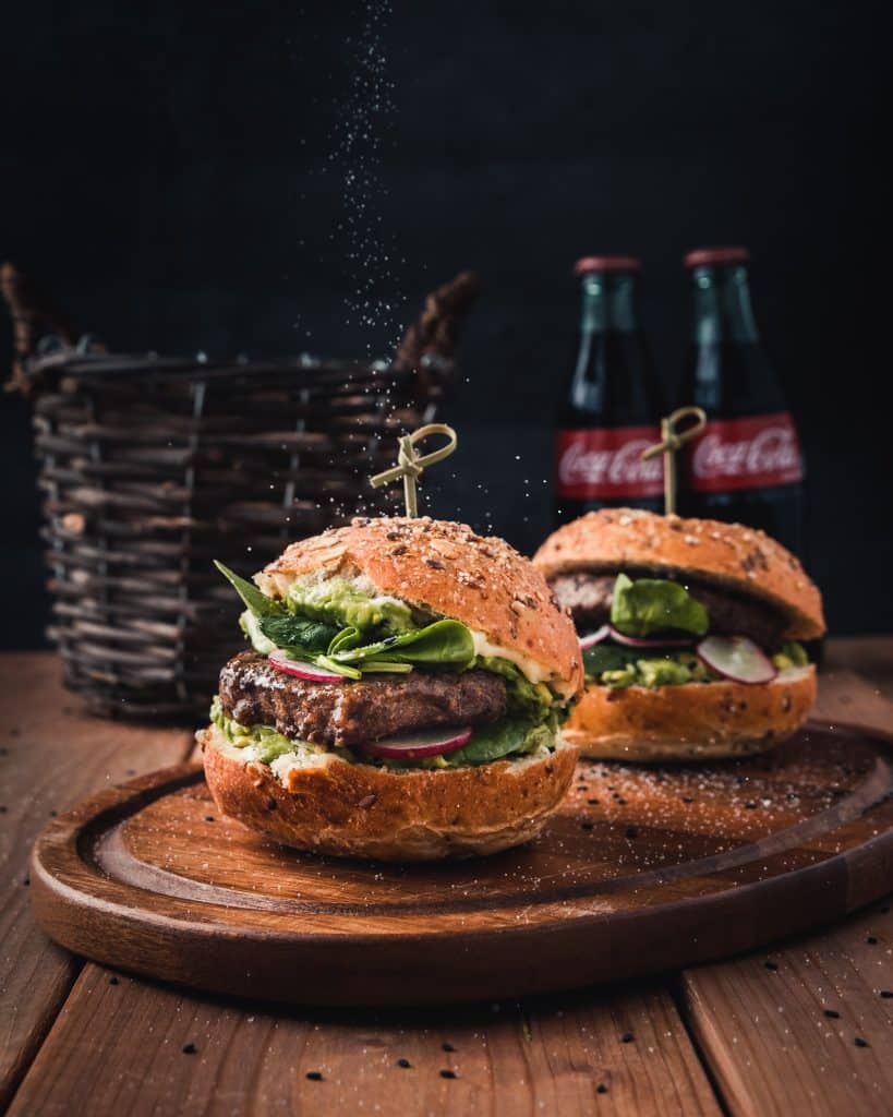 food photography of salt being sprinkled over hamburgers with coke bottles in the background