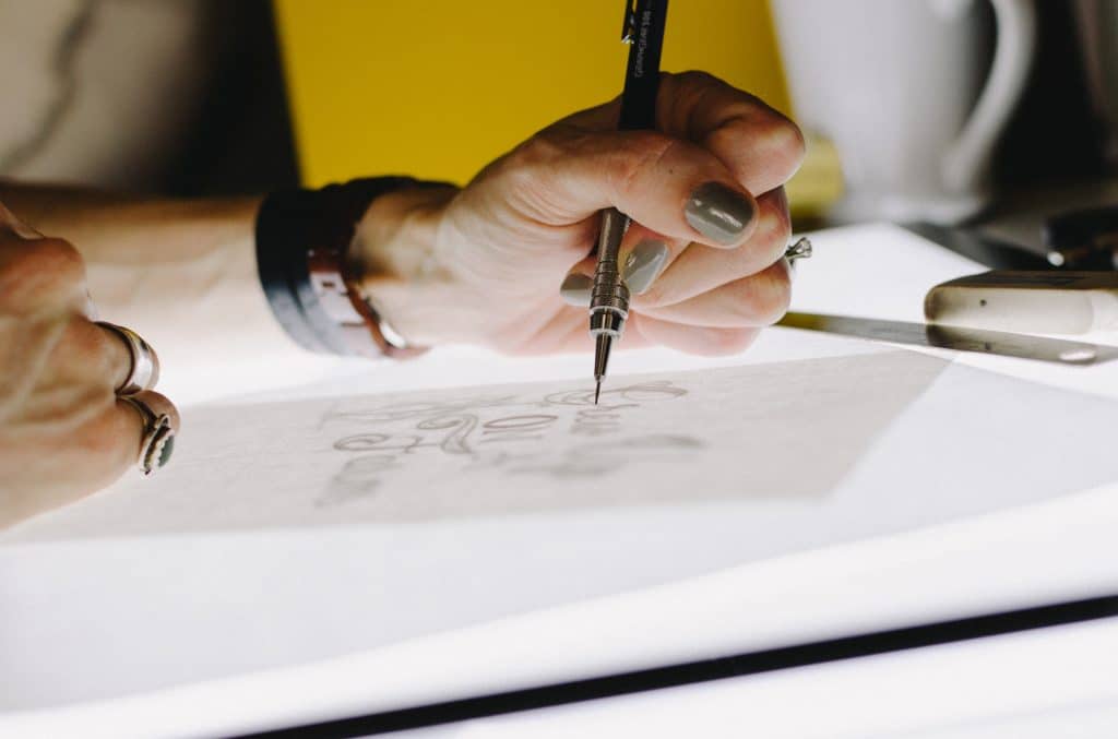 Woman wearing a watch and rings with green and nail polish tracing on a lightbox. There is a yellow background.
