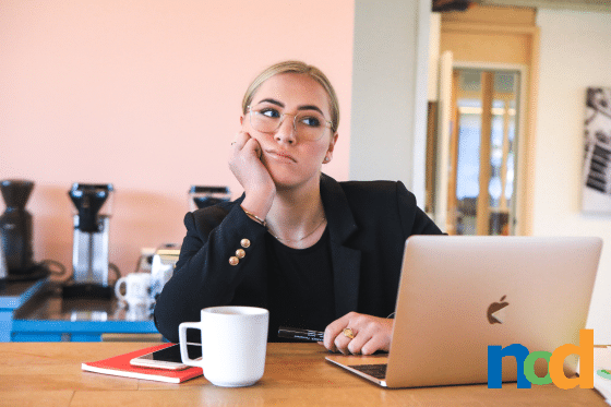 Woman wearing a suit sitting in front of a laptop with a white coffee cup