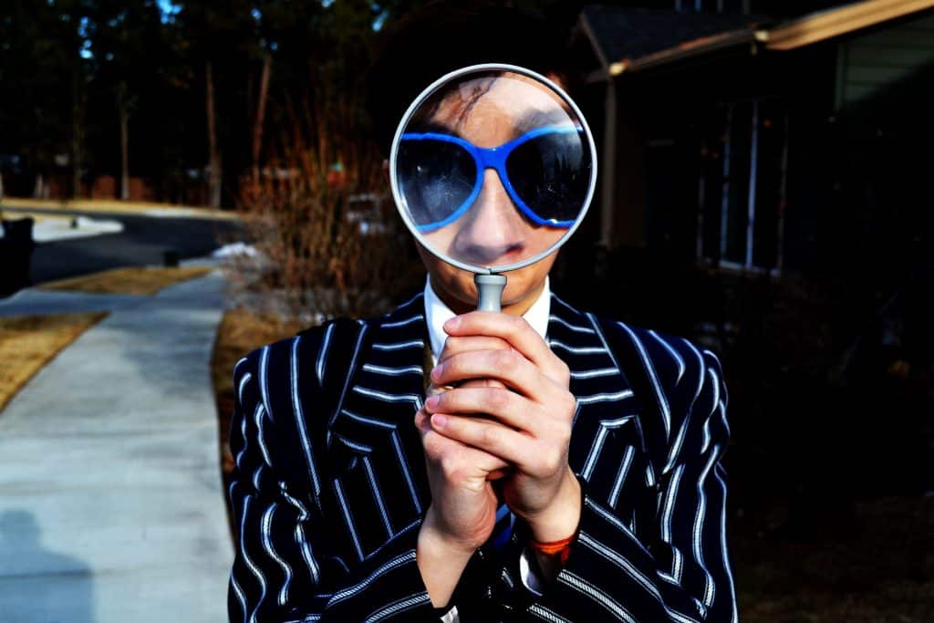 Woman with striped blazer and sunglasses looking through a magnifying glass