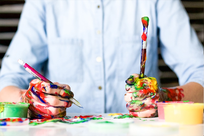 messy hands holding pencil and paintbrush