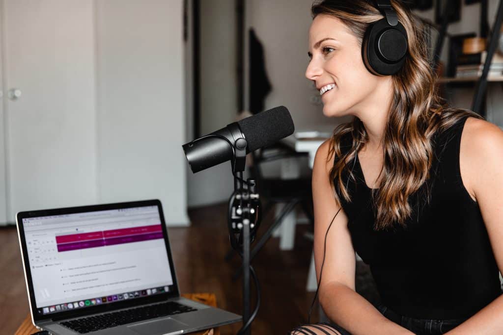 Woman wearing headphones speaking into a microphone in front of a laptop
