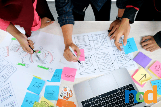 Three people brainstorming user experience on paper, facing a laptop.